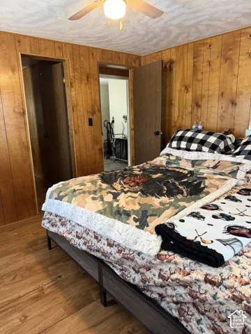 Wood-finish wall paneling, wood-finish flooring, and a ceiling fan with integrated lighting