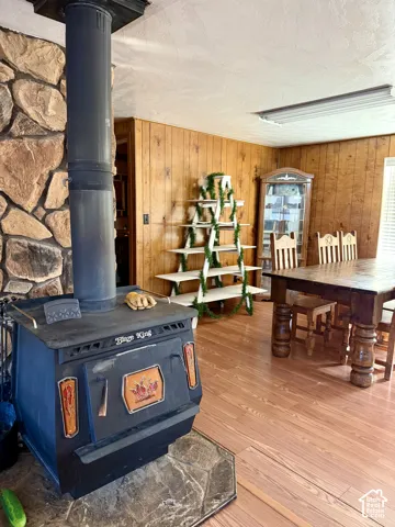 Stone-faced wood-burning stove with a stone hearth, wood-paneled accent wall, and wood-finish flooring