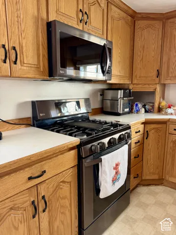 Wood cabinetry with black hardware, stainless steel microwave, stainless steel range, and light-toned countertops