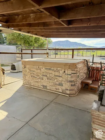 Covered patio featuring a stone-clad spa, wood steps, and concrete flooring