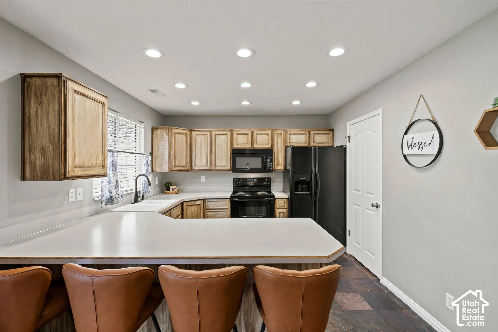 Kitchen featuring recessed lighting, light-toned cabinetry, a corner sink with a black faucet, black appliances, and tile flooring