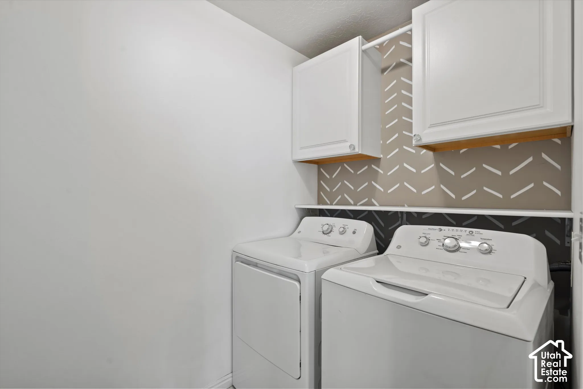 Laundry area with white cabinetry, a built-in shelf, and a patterned accent wall