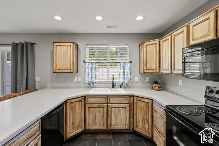 Kitchen featuring wood-finish cabinetry, light-toned countertops, and a black appliance suite including a built-in microwave and electric range