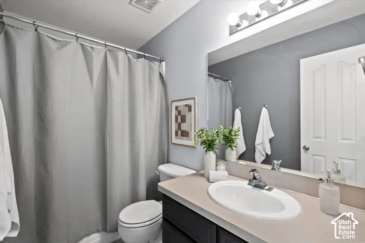 Bathroom featuring a single vanity with an oval sink, a light-toned countertop, a large wall-mounted mirror, overhead vanity lighting, and a white toilet