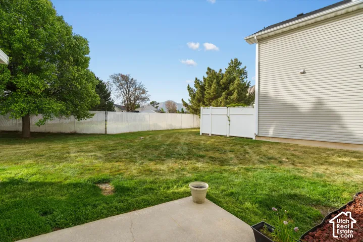Expansive grassy yard with mature trees, a fence, and a concrete patio
