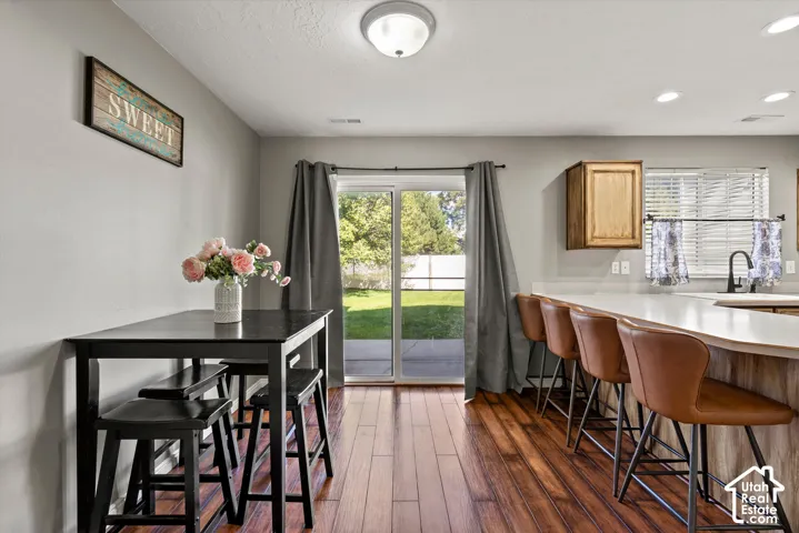 Wood-finish flooring throughout, sliding glass door with yard access, kitchen island with seating, recessed ceiling lights, and sink steel sink with a gooseneck faucet