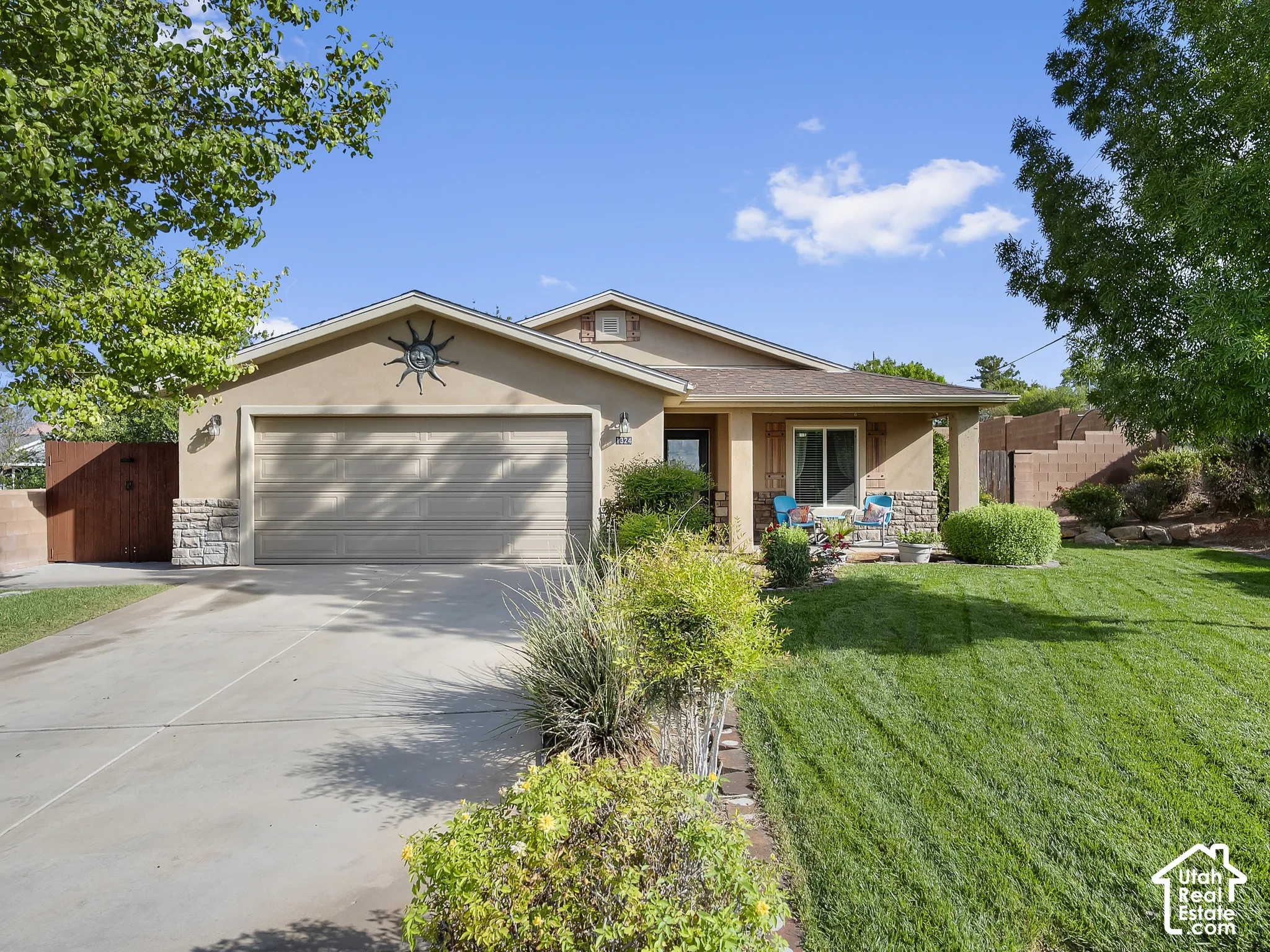 Stucco exterior with stone accents, attached two-car garage, concrete driveway, front porch, and mature landscaping