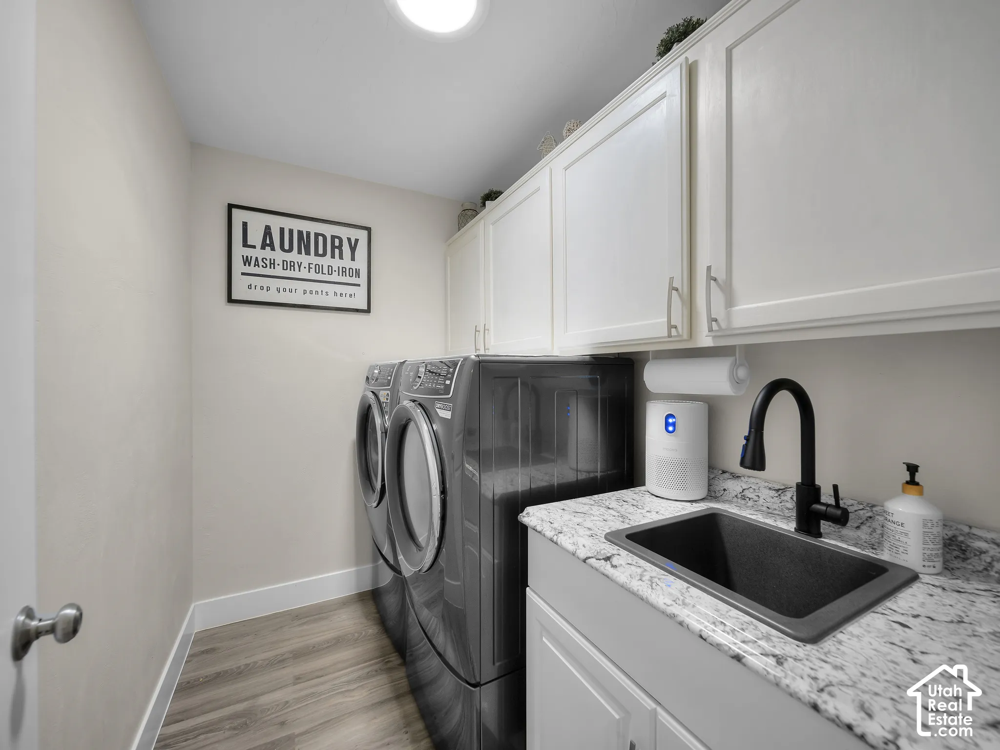 Wood-finish flooring, white cabinetry, speckled countertop, undermount sink, and a matte black faucet