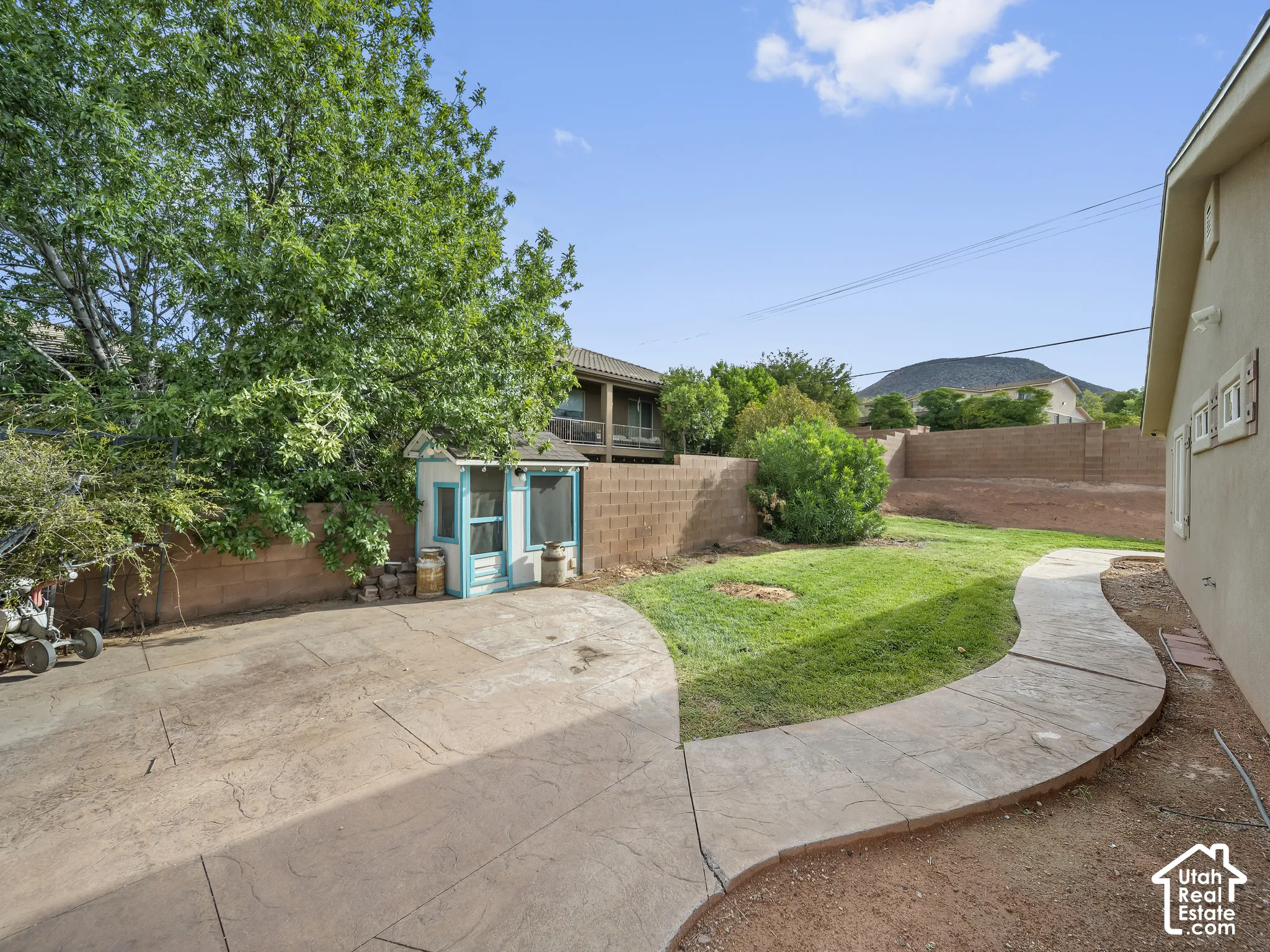 Expansive backyard featuring a concrete patio, landscaped grass area, concrete pathway, and a detached structure