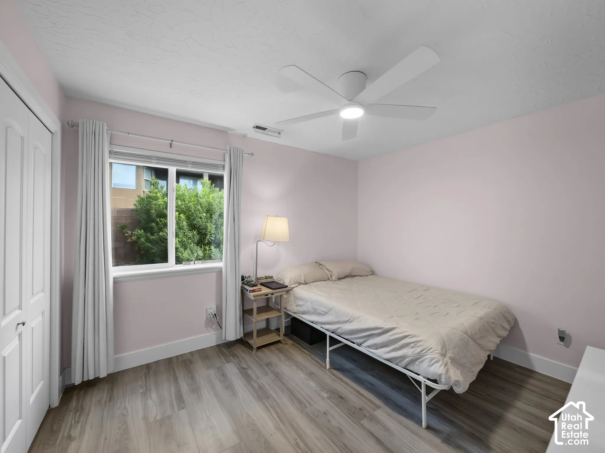 Wood-finish flooring, white ceiling fan with integrated lighting, window with white trim, and a white paneled closet door