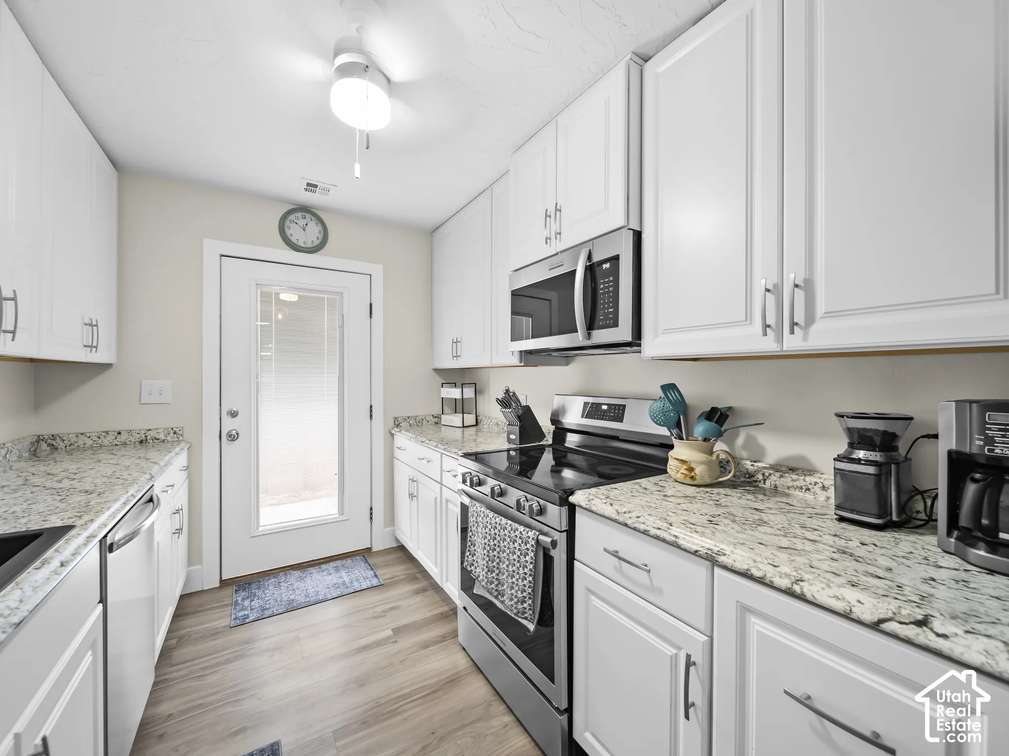 Kitchen with wood-finish flooring, white cabinetry, speckled countertops, stainless steel appliances, and a glass-paneled door