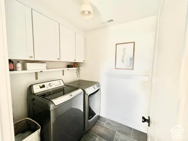 Laundry area featuring white cabinetry, a floating shelf with brass-finish brackets, and dark-toned tile flooring