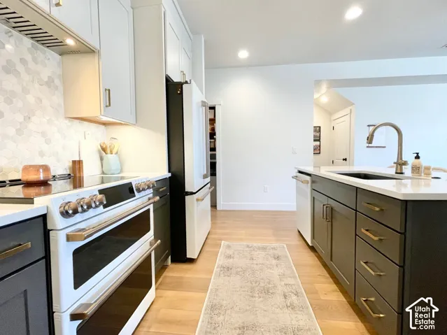 Kitchen featuring light-finish flooring, two-tone cabinetry, hexagon tile backsplash, recessed lighting, and a kitchen island with an undermount sink