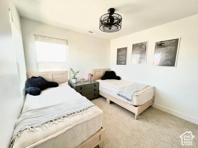 Recessed window with roller shade, white walls, textured carpeting, and a black ceiling fan with a caged design