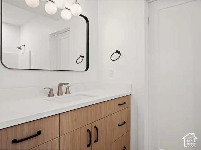 Wood-finish vanity with black hardware, white countertop, rectangular undermount sink, and brushed nickel faucet