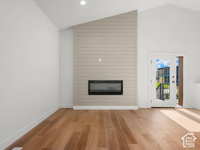 Wood-finish flooring with an electric fireplace, shiplap accent wall, and vaulted ceiling