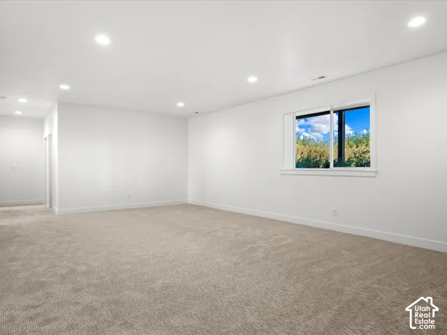 Spacious room featuring neutral carpeting, recessed lighting, and a window with white trim