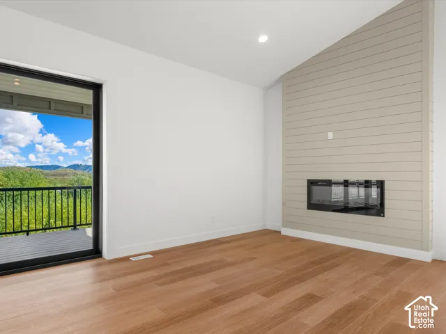 Wood-finish flooring, full-height glass door, black balcony railing, built-in fireplace, and vaulted ceiling