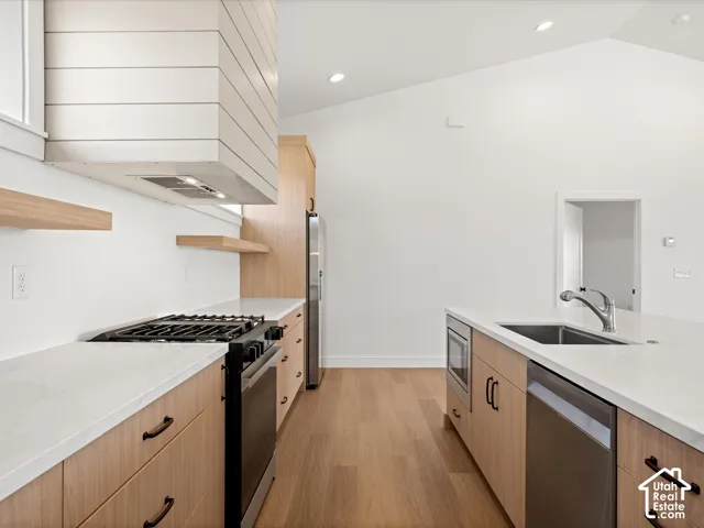 Vaulted ceilings with recessed lighting, wood-finish flooring, white countertops, built-in stainless steel appliances, and wood cabinetry with black hardware