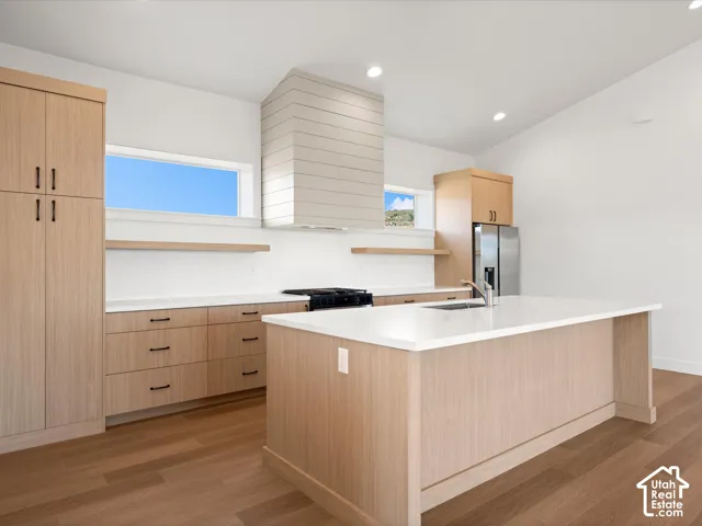 Modern kitchen featuring light wood-finish cabinetry, white countertops, stainless steel appliances, and wood-finish flooring