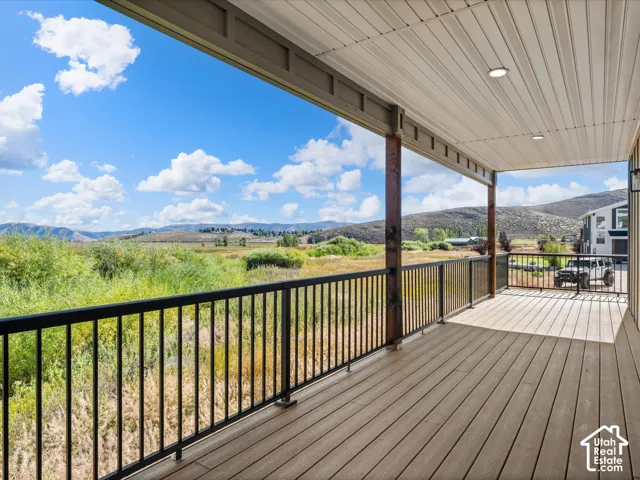 Expansive covered deck with composite wood-finish flooring, recessed lighting, and black metal railings