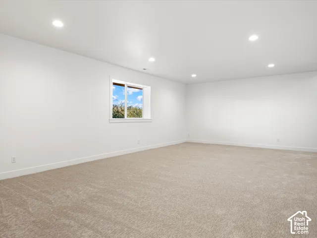 Spacious room with plush carpet flooring, recessed ceiling lighting, a white framed window, and white painted walls