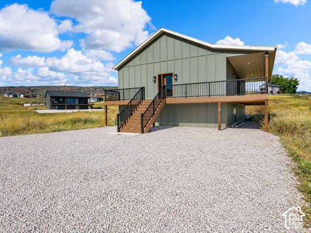 Modern exterior featuring vertical siding, an elevated wood-finish deck with black railings, and a gravel driveway