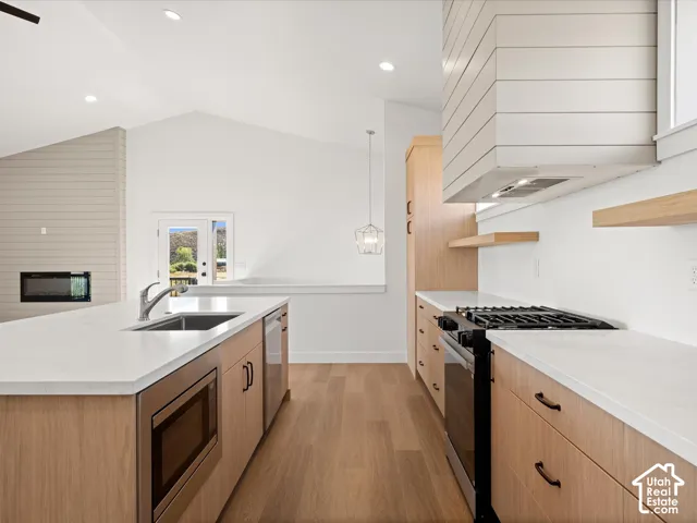 Vaulted ceilings, wood-finish flooring, light wood cabinetry, white countertops, and a built-in microwave