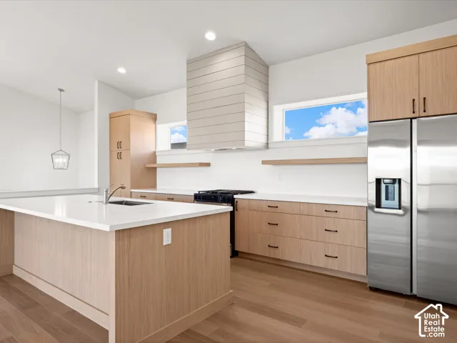 Kitchen featuring an expansive island with an undermount sink, wood-finish cabinetry, stainless steel appliances, and wood-finish flooring