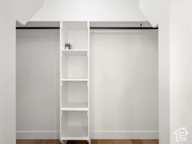 Built-in closet system featuring white shelving, black hanging rods, and wood-finish flooring