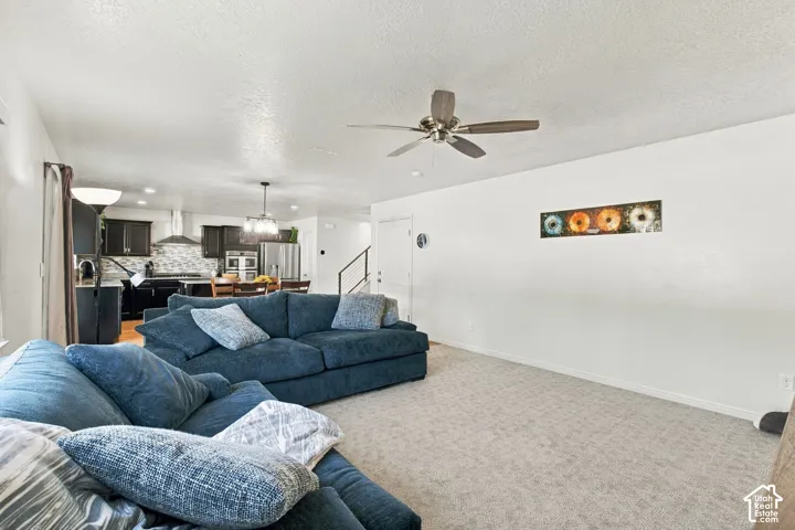 Open-concept living space with light-toned carpeting and a ceiling fan
