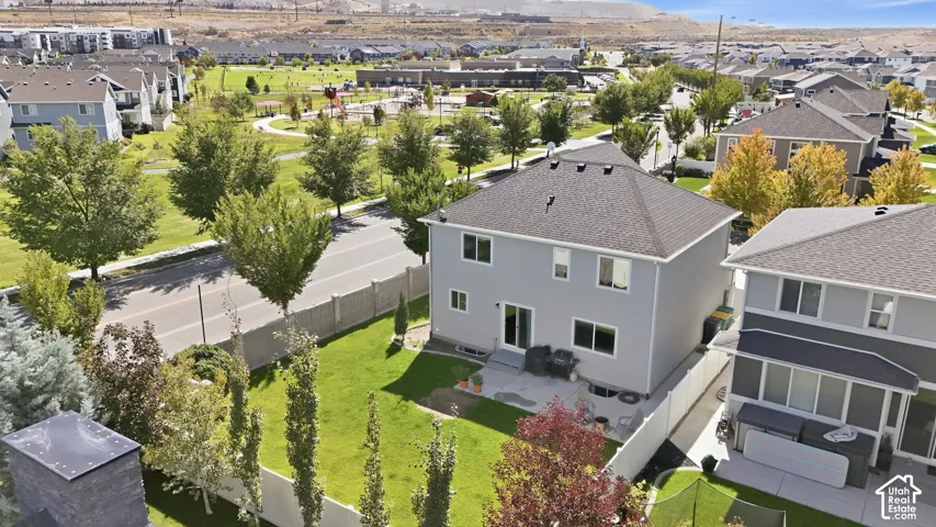 Rear exterior featuring a patio, manicured lawn, and mature trees
