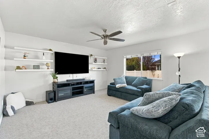 Spacious living area featuring carpet flooring, built-in wall shelves, a ceiling fan with integrated lighting, and a large window
