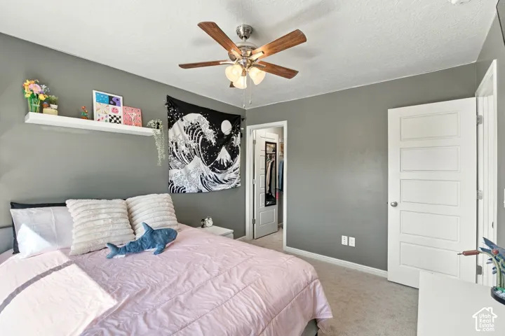 Carpeted bedroom featuring a ceiling fan with light fixture, a floating wall shelf, and a closet with a built-in organizer