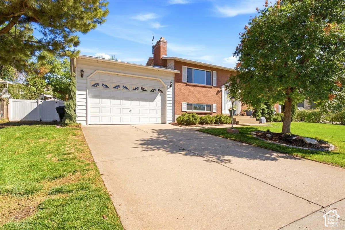 Brick exterior with white trim, attached garage with decorative windows, concrete driveway, and mature landscaping