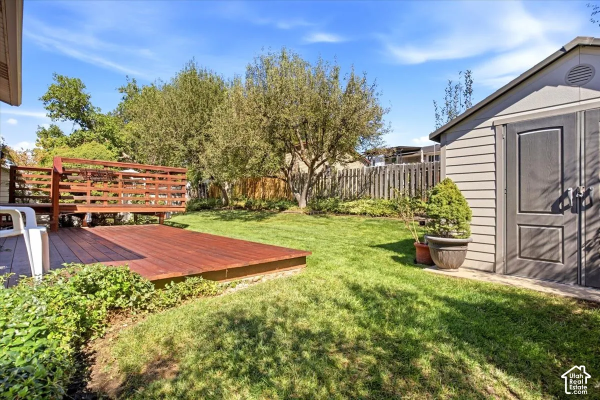 Expansive backyard featuring a wood-finish deck with railing, a detached storage shed, a manicured lawn, and mature trees
