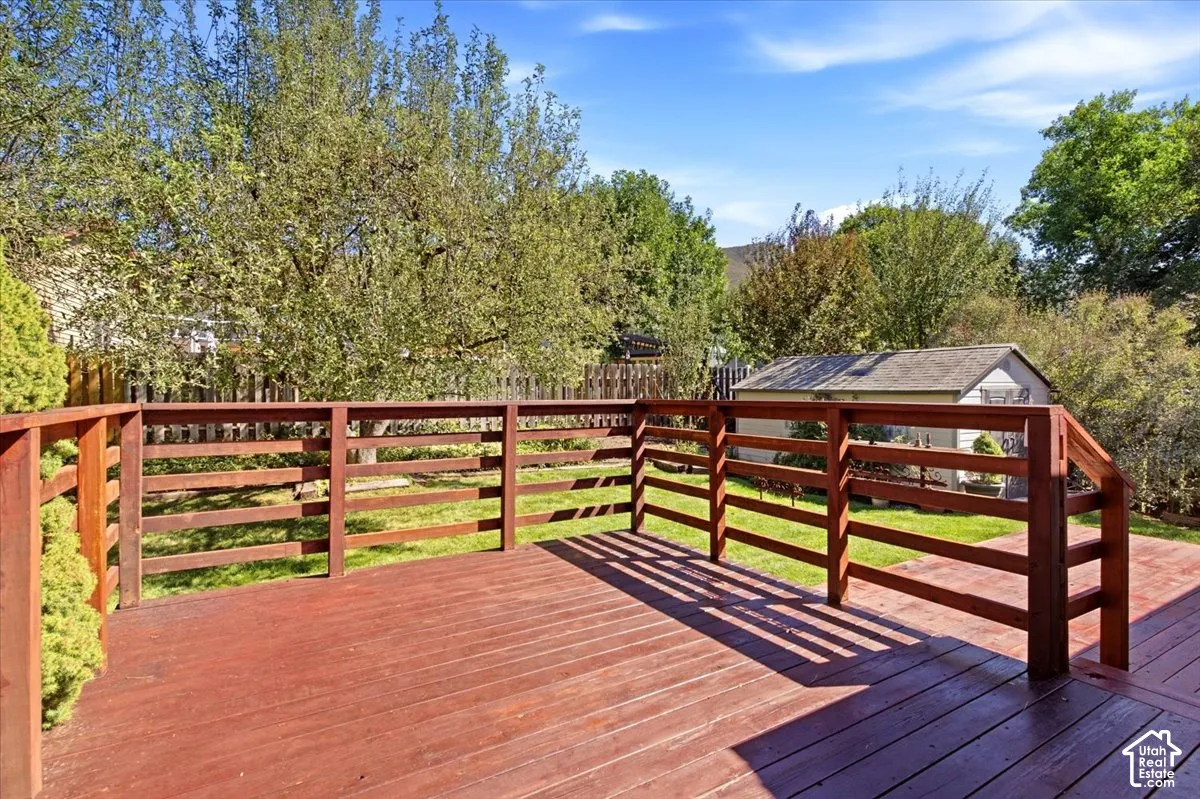 Expansive wood deck with a horizontal slatted railing, overlooking a verdant lawn and mature trees