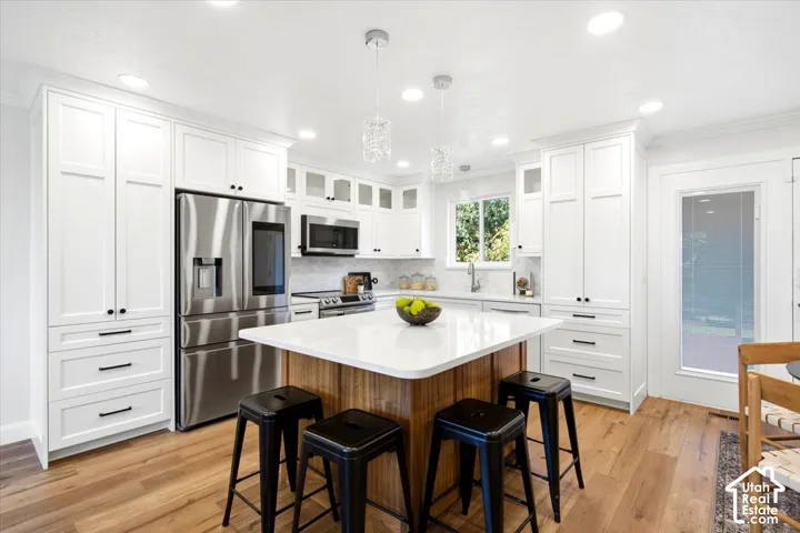 White cabinetry, wood-finish flooring, stainless steel appliances, central kitchen island, and recessed lighting