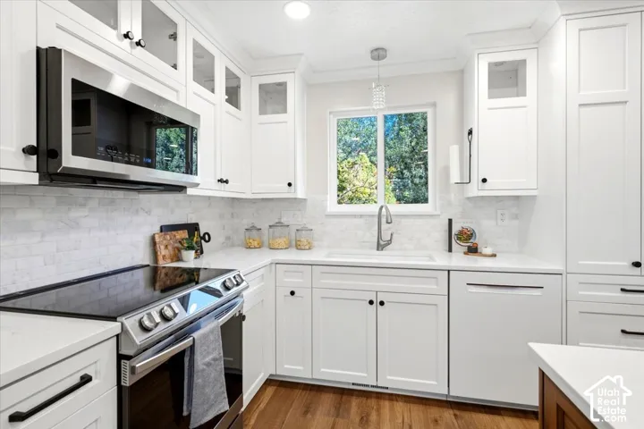 White shaker-style cabinetry with black hardware, stainless steel appliances, a white tile backsplash, and wood-finish flooring