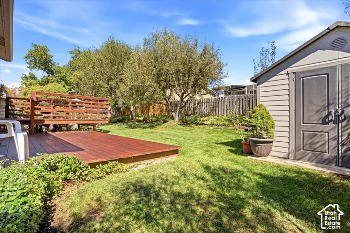 Expansive backyard featuring a wood-finish deck with railing, a detached storage shed, a manicured lawn, and mature trees