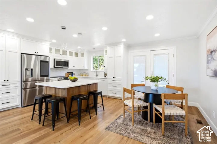 Wood-finish flooring, white cabinetry with black hardware, stainless steel appliances, central island with seating, and glass panel doors