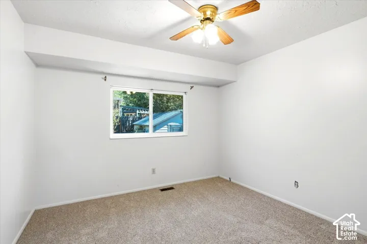 Neutral-toned carpeting paired with white walls, a single window, and a ceiling fan with light fixture
