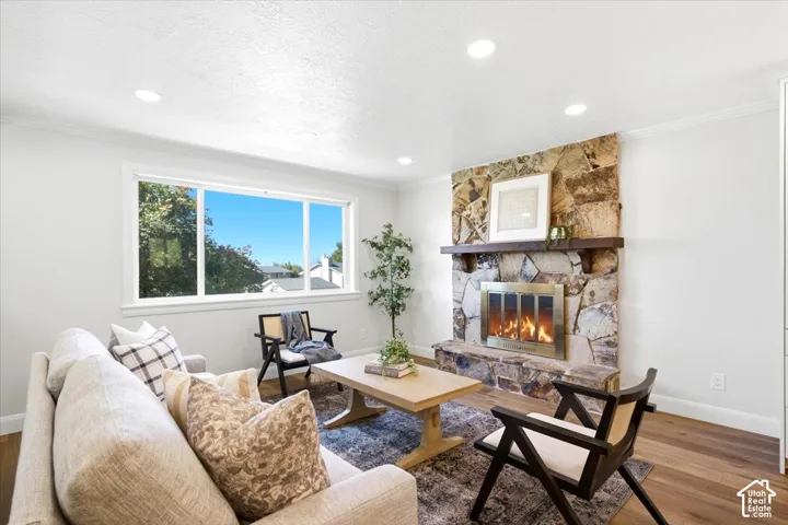 Expansive picture window, recessed ceiling lighting, stone-clad fireplace with wood mantel, hardwood flooring, and neutral wall tones