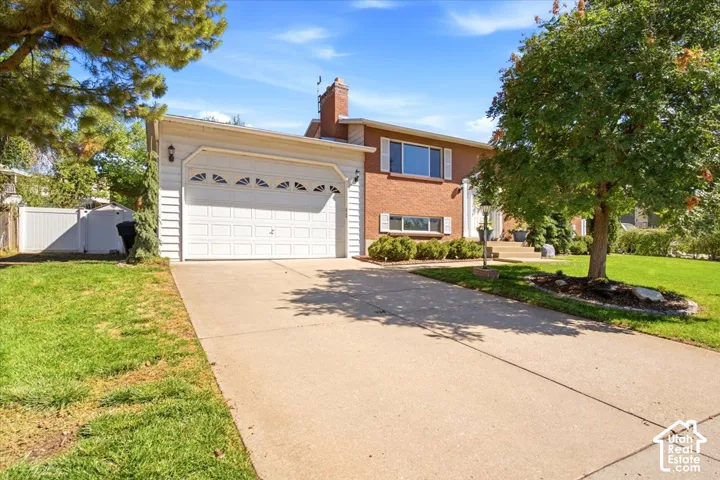 Brick exterior with white trim, attached garage with decorative windows, concrete driveway, and mature landscaping