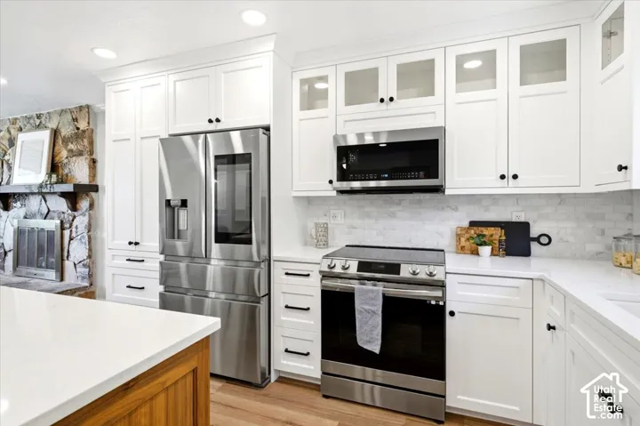 White shaker cabinetry, stainless steel appliances, recessed lighting, stone backsplash, and light-toned countertops