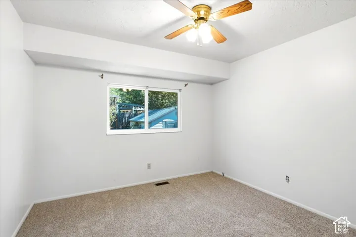 Neutral-toned carpeting paired with white walls, a single window, and a ceiling fan with light fixture