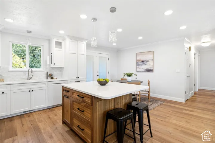 Kitchen with wood-finish flooring, white cabinetry, a white countertop island with wood-finish base, and recessed lighting