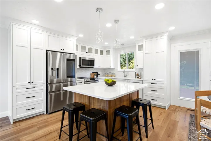 White cabinetry, wood-finish flooring, stainless steel appliances, central kitchen island, and recessed lighting