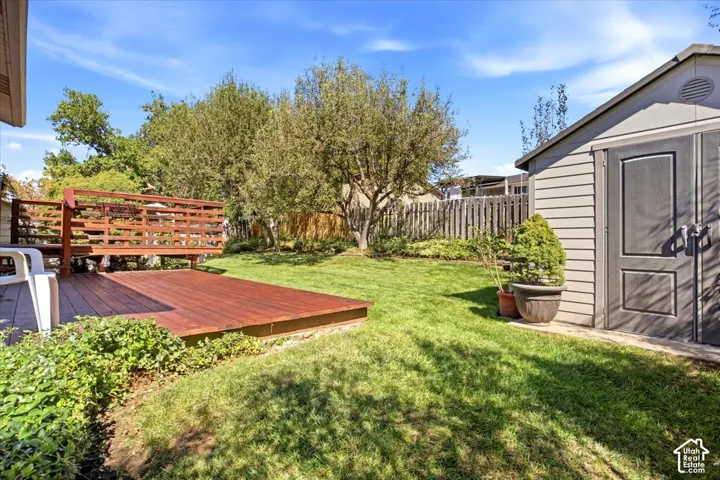 Expansive backyard featuring a wood-finish deck with railing, a detached storage shed, a manicured lawn, and mature trees