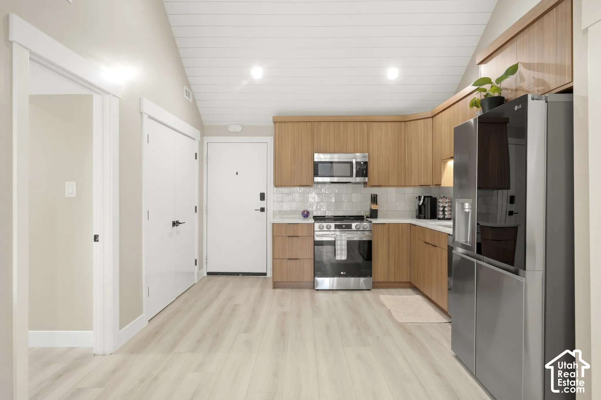 Modern kitchen featuring wood-finish cabinetry, stainless steel appliances, a tile backsplash, and light wood-finish flooring